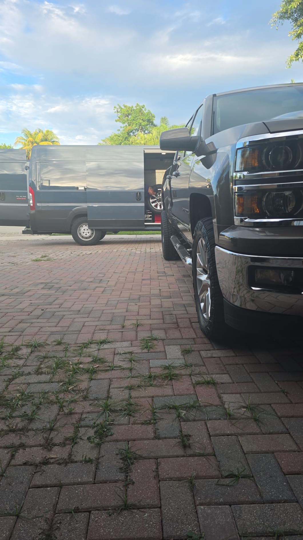 Front corner of a dark grey Chevrolet Silverado on Patagonia tires, parked on brick pavers beside a mobile tire-fitting van