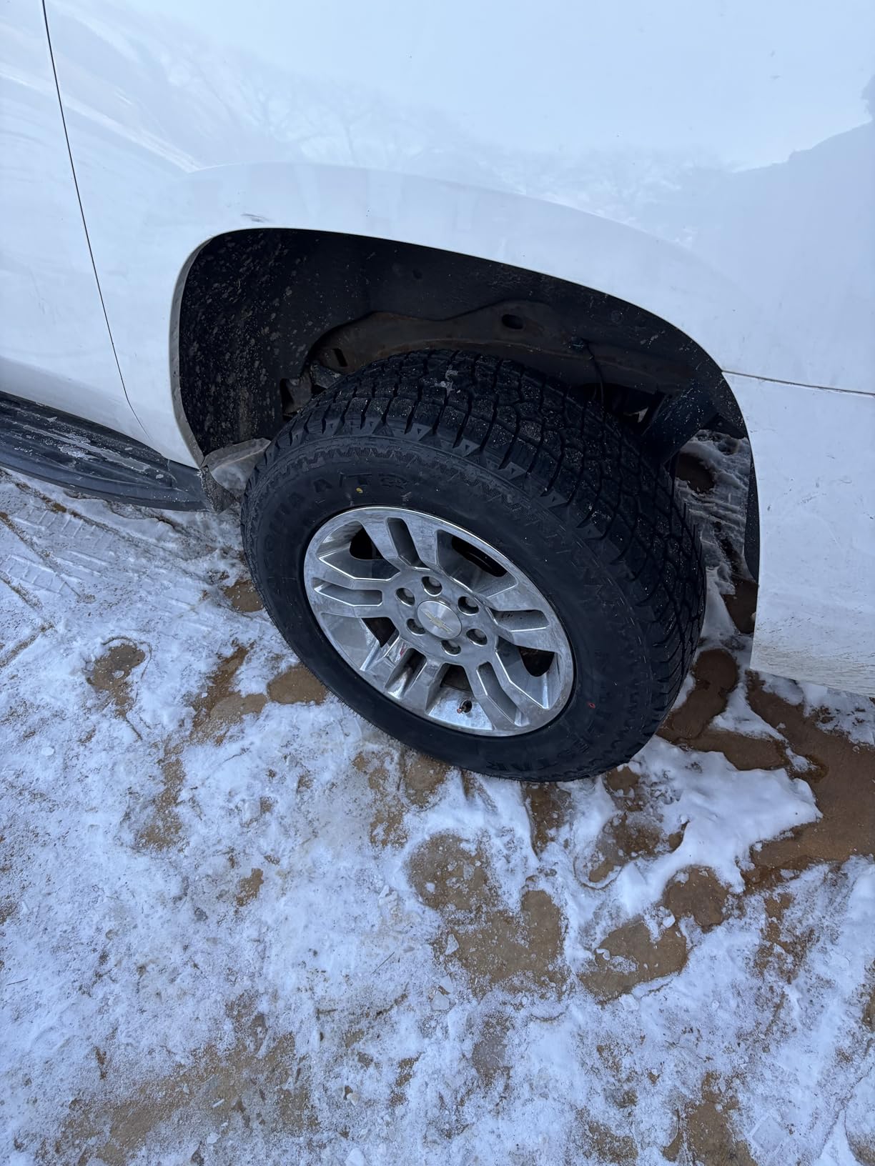 Front wheel of a white Chevrolet Silverado on a Patagonia A/T, parked on packed snow and slush