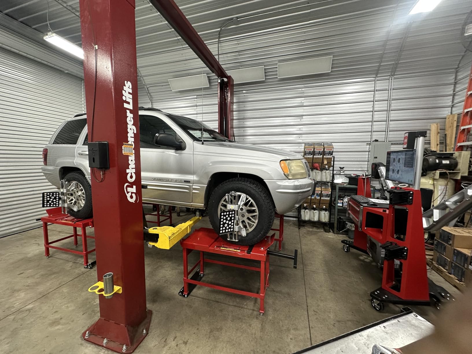 Silver Jeep Grand Cherokee raised on a two-post lift in an alignment bay, all-terrain tires on the wheel stands