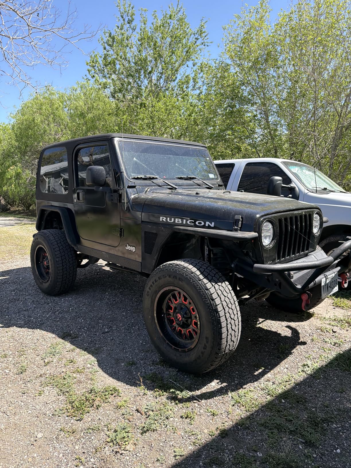 Black Jeep Wrangler Rubicon on Milestar Patagonia tires and red and black off-road wheels, parked on a gravel lot