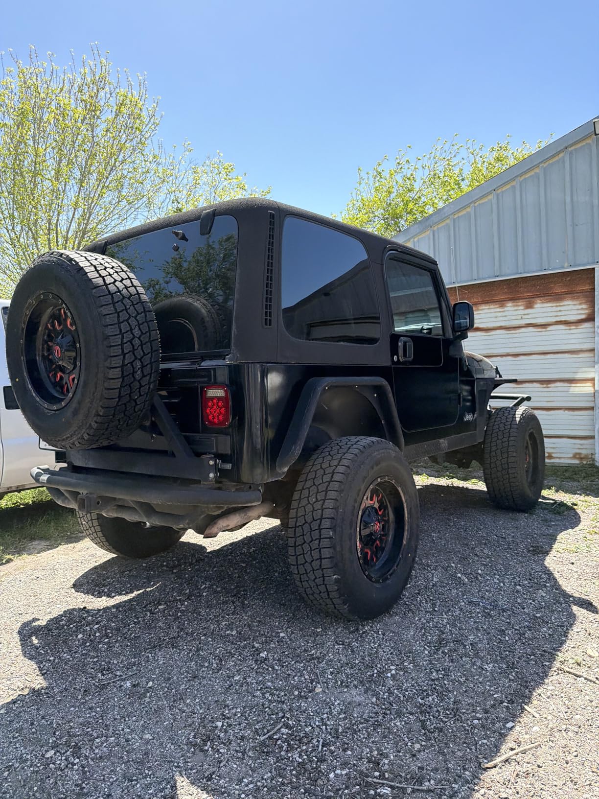 Rear three-quarter of a lifted black Jeep Wrangler Rubicon, tailgate spare and all four corners on Patagonia all-terrain tires